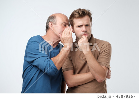 Senior man sharing secret or whispering gossips into his son ear. Telling family secret concept 45879367