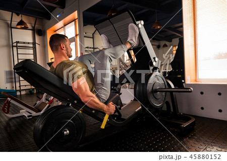 Young sporty man does leg exercises in gym side view Young sporty man does leg exercises in gym side view 45880152
