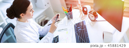 A young girl in the office sits at a table, holds a marker and a pencil in her hand and works with a A young girl in the office sits at a table, holds a marker and a pencil in her hand and works with a 45881429