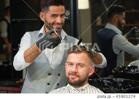 Barber doing trendy haircut to young man in barber shop 45901274