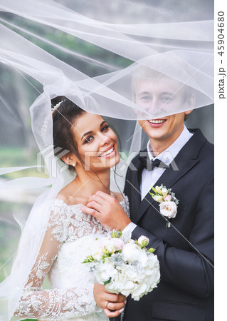 Happy bride and groom in a park hugging under veil. Wedding couple in love Happy bride and groom in a park hugging under veil. Wedding couple in love 45904680
