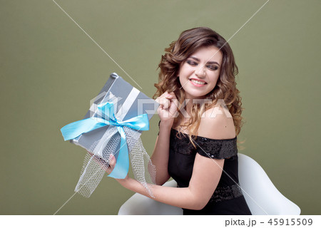 Fun woman holding above her head striped present box with ribbon isolated on green background. For 45915509