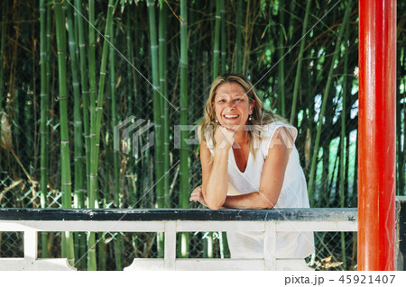 Smiling woman leaning on fence by bamboo Smiling woman leaning on fence by bamboo 45921407