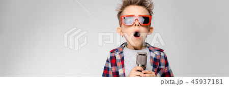 A handsome boy in a plaid shirt, gray shirt and jeans stands on a gray background. A boy wearing A handsome boy in a plaid shirt, gray shirt and jeans stands on a gray background. A boy wearing 45937181