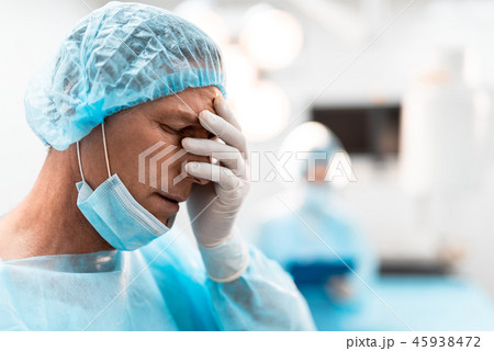 Exhausted doctor putting hand on his face while feeling tired Exhausted doctor putting hand on his face while feeling tired 45938472