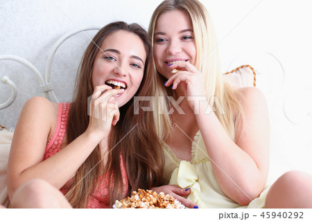 Two happy smiling girlfriends eat popcorn in bed 45940292