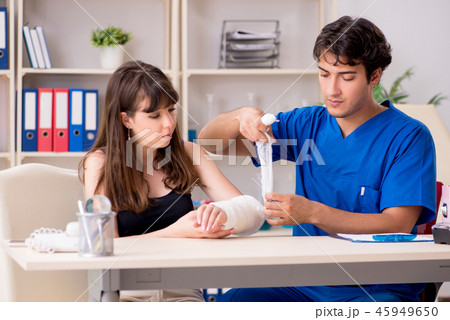 Young woman with bandaged arm visiting male doctor traumotologis Young woman with bandaged arm visiting male doctor traumotologis 45949650