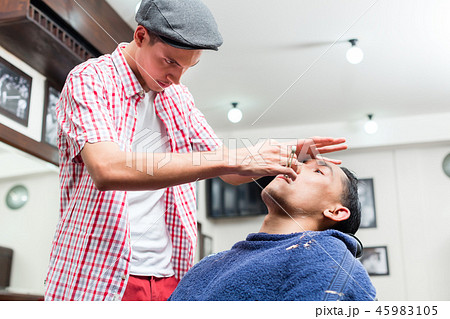 Male barber wearing baseball cap shaving with razor Male barber wearing baseball cap shaving with razor 45983105