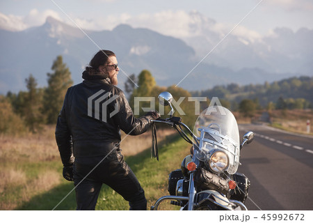 Tall athletic biker in black leather clothing standing at modern powerful high-speed motorcycle. 45992672