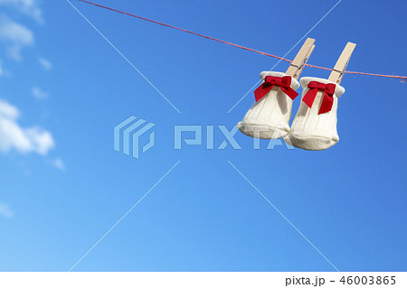 青空に木製洗濯挟みで吊るされた赤いリボンの新生児用靴下。赤ちゃん、育児、出産、幸せ、愛イメージ 46003865