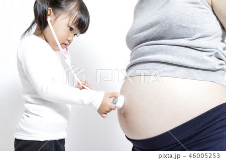 妊娠したお母さんの大きなお腹を玩具の聴診器で診察する女の子の手元のアップ 妊娠 臨月 親子 遊び 生の写真素材