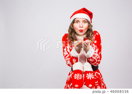 People, christmas and holidays concept - pretty young lady in santa claus costume blowing confetti 46008336