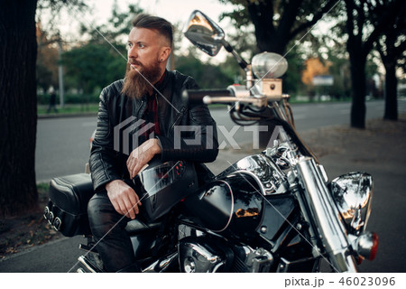 Baerded biker poses on chopper leaning on a helmet 46023096