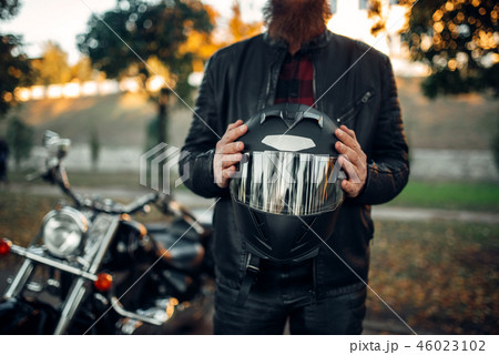 Biker holds helmet in hands, chopper on background 46023102