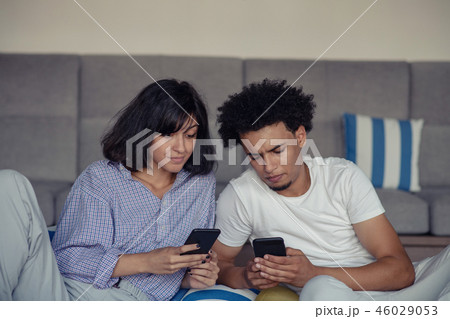 Relaxed couple or friends using a generic mobile phone together sitting on a sofa in the living room Relaxed couple or friends using a generic mobile phone together sitting on a sofa in the living room 46029053