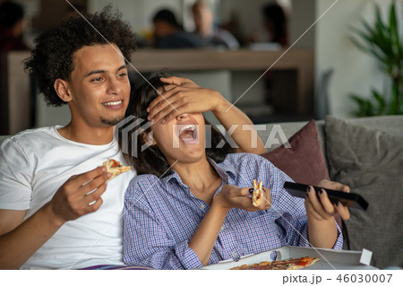 Happy couple watching tv while eating pizza. Shallow depth of field, focus on the man 46030007