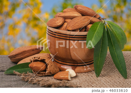 almonds in a bowl on the old wooden board with sackcloth and blurred garden background 46033610