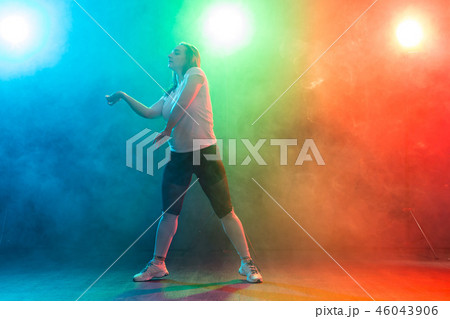 Dance, sport, and people concept - young woman dancing in the darkness under colourful light 46043906