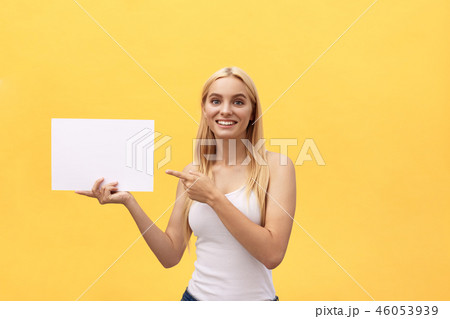 Young woman over yellow background holding blank paper sheet with surprise face pointing finger copy 46053939