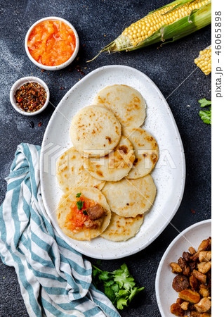 COLOMBIAN FOOD. Maize AREPAS and fried pork chicharron ans colombian tomato sauce. Top view. Black COLOMBIAN FOOD. Maize AREPAS and fried pork chicharron ans colombian tomato sauce. Top view. Black 46065898