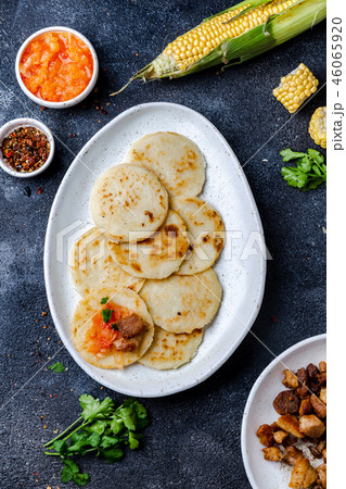 COLOMBIAN FOOD. Maize AREPAS and fried pork chicharron ans colombian tomato sauce. Top view. Black COLOMBIAN FOOD. Maize AREPAS and fried pork chicharron ans colombian tomato sauce. Top view. Black 46065920