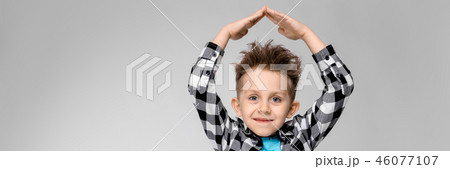 A handsome boy in a plaid shirt, blue shirt and jeans stands on a gray background. The boy folded 46077107