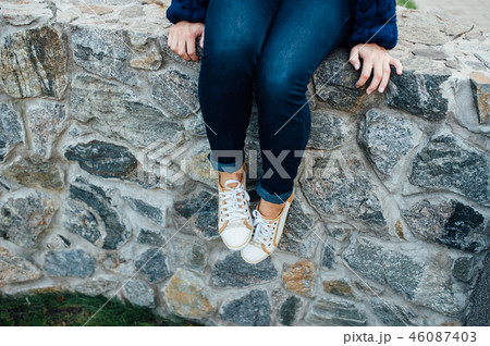 woman's legs with sneakers seated in stone wall. 46087403