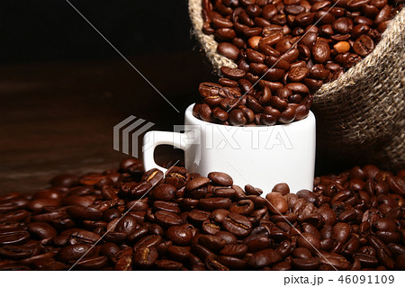 Fresh roasted coffee beans in burlap sack, coffee cup and grinder on dark background. Fresh roasted coffee beans in burlap sack, coffee cup and grinder on dark background. 46091109