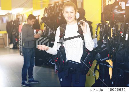Female is standing with modern diving vest in the store. Female is standing with modern diving vest in the store. 46096632