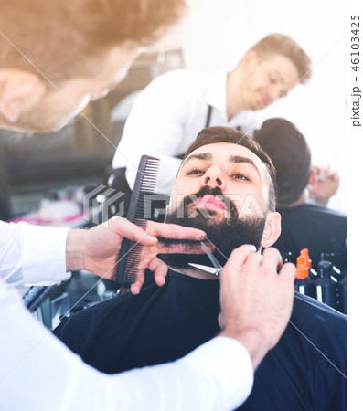 Male hairdresser accurately cutting beard of client Male hairdresser accurately cutting beard of client 46103425