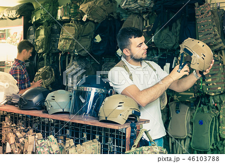 Young guys choosing helmet in military shop Young guys choosing helmet in military shop 46103788
