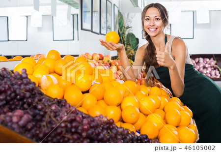 Cheerful woman seller holding orange in hand 46105002