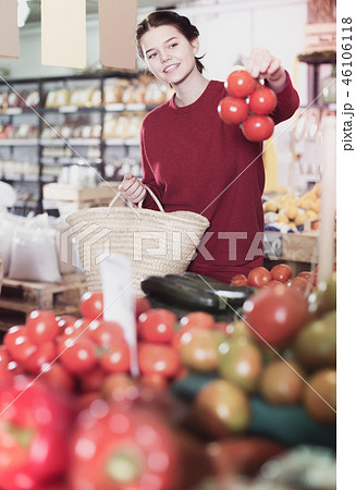 Portrait of positive young female customer selecting tomatoes in grocery 46106118