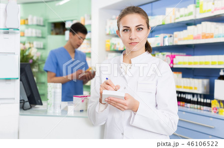 Young female pharmacist is attentively checking medicine to notebook 46106522