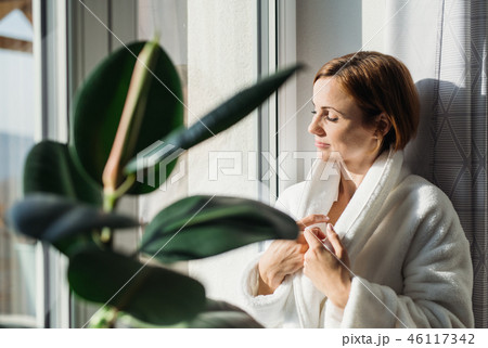 A young woman with bath robe standing indoors by a window in the morning. 46117342