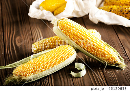 Kitchen table with raw and grilled sweet corn cob 46120653