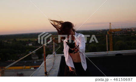 Young girl in sports uniform sits on the edge of the roof during sunset. Young girl in sports uniform sits on the edge of the roof during sunset. 46150697