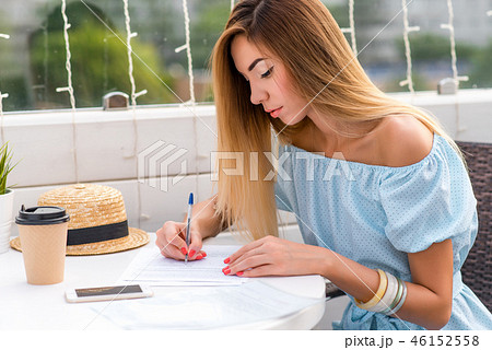 Beautiful girl in blue dress, tanned skin with long hair. Summer sitting in a cafe. He holds a pen Beautiful girl in blue dress, tanned skin with long hair. Summer sitting in a cafe. He holds a pen 46152558