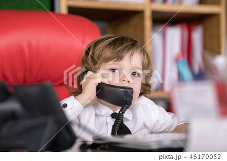 Little boy sits in the office in the chair and talking on the phone. Little boss. Little boy sits in the office in the chair and talking on the phone. Little boss. 46170052