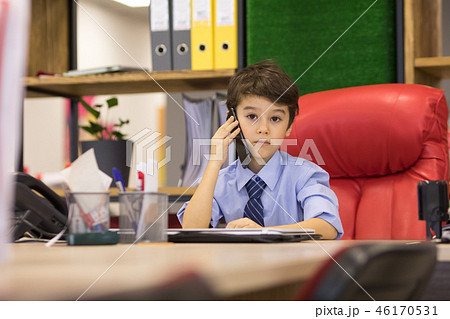 Boy sits in the office in the chair and talking on the phone. Little boss. 46170531