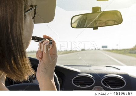 Girl driving a car puts lipstick while driving. 46196267