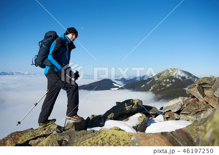 Hiker on rocky hill on background of valley with white clouds, snowy mountains and blue sky. Hiker on rocky hill on background of valley with white clouds, snowy mountains and blue sky. 46197250