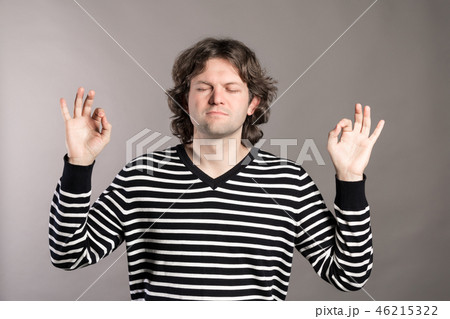 Peaceful young man meditating with his eyes closed and keeping hands in mudra gesture. Handsome guy Peaceful young man meditating with his eyes closed and keeping hands in mudra gesture. Handsome guy 46215322