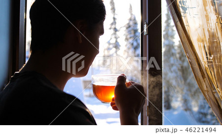 Winter frosty day. The guy early in the morning standing at the window and drinking hot tea. Winter frosty day. The guy early in the morning standing at the window and drinking hot tea. 46221494