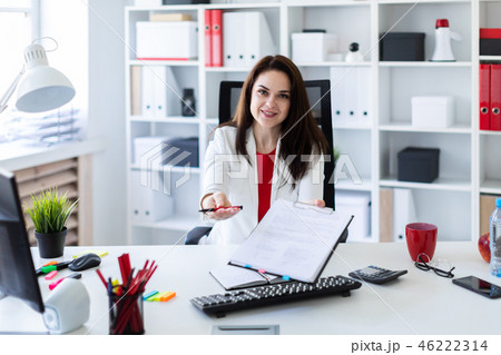 A young girl sitting in the office at a computer Desk and stretches forward a pen and a sheet. 46222314