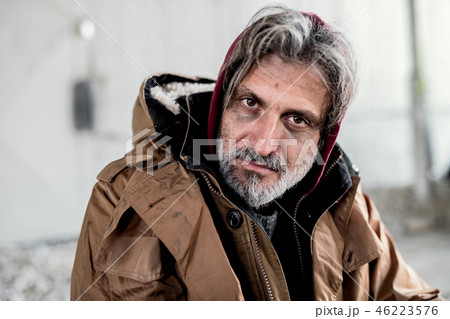 A portrait of homeless beggar man sitting outdoors. 46223576