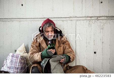 A front view of homeless beggar man sitting outdoors, holding bottle of alcohol. Copy space. 46223583