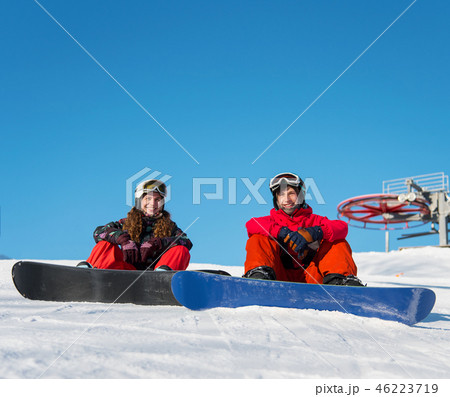 Guy and girl snowboarders are sitting on the snow at the top of the ski slope against the blue sky 46223719