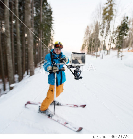 Skier man taking selfie with stick over forest on the winter resort. Focus on his camera Skier man taking selfie with stick over forest on the winter resort. Focus on his camera 46223720