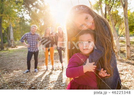Mixed Race Young Sisters Hug with Family Behind Mixed Race Young Sisters Hug with Family Behind 46225348